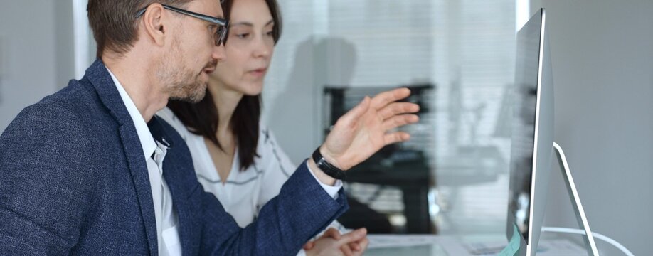Colleagues collaborating, man pointing at desktop computer screen, woman listening during business discussion in office. Businesspeople concept