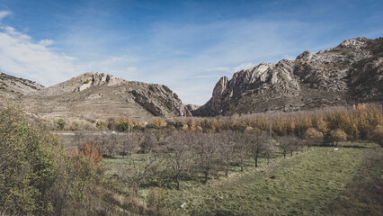 Panoramic view of a mountain valley with bare autumn trees and rocky hills under a clear blue sky. Natural rural landscape in Spain.