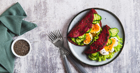 Beetroot chia pancakes with poached egg, cucumber and lettuce on a plate top view web banner