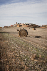 Close-up of a single hay bale on dry farmland after harvest, with a small town visible in the background.