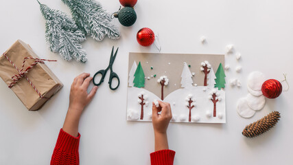 Child's hands crafting a winter scene with paper, cotton, and decorations