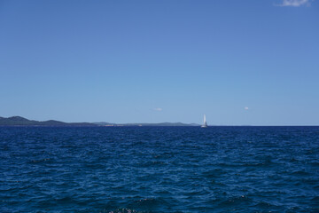 White boat far off on vivid blue sea under a bright sunny sky &mdash; minimalistic marine scene capturing calm water and distant horizon
