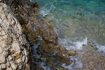 Close-up of a rocky shoreline by the bright blue waters of the Adriatic Sea on a sunny summer day — textured stones meet the sparkling sea in a vivid, natural coastal moment.