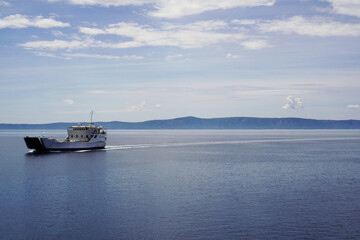 A ship sailing on the open sea with a mountainous coastline in the background on a bright sunny day.