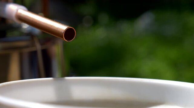 Copper tube with drops of distilled water emerging from it. Flower distillation. A natural process. Slow motion 4K