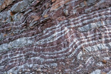A detailed close-up of a layered rock face, showing alternating bands of reddish-brown and gray-white minerals