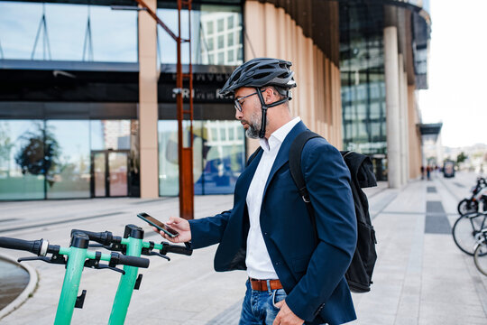 Businessman unlocking electric scooter with smartphone.