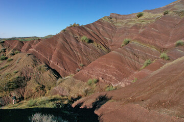 Layered rock formations of the Zagros Mountains, featuring distinctive red and green sedimentary strata under a clear sky in Kurdistan