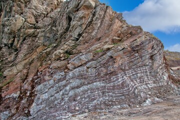 Naklejka premium Layered rock formations of the Zagros Mountains, featuring distinctive red and green sedimentary strata under a clear sky in Kurdistan