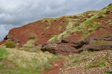 Layered rock formations of the Zagros Mountains, featuring distinctive red and green sedimentary strata under a clear sky in Kurdistan