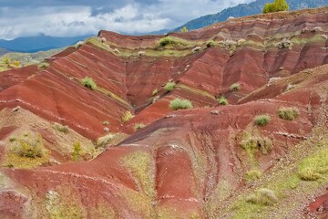 Layered rock formations of the Zagros Mountains, featuring distinctive red and green sedimentary strata under a clear sky in Kurdistan