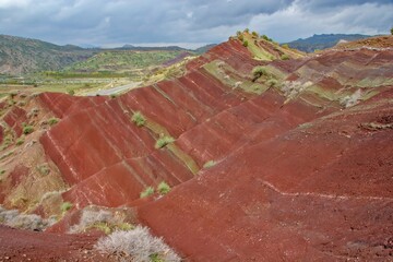 Layered rock formations of the Zagros Mountains, featuring distinctive red and green sedimentary strata under a clear sky in Kurdistan