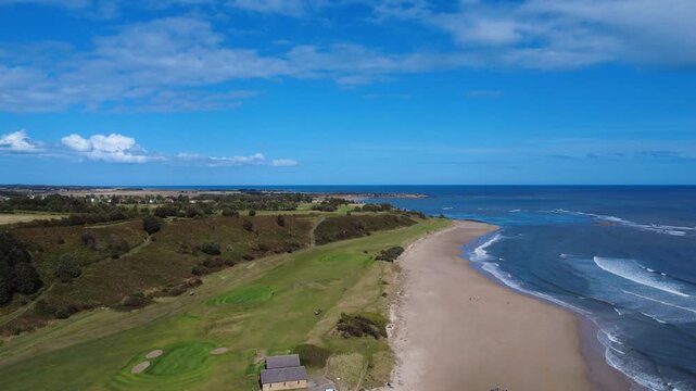 Aerial panoramic view of Alnmouth beach in bright summer sunlight with waves on the blue sea and surrounding coastal landscape