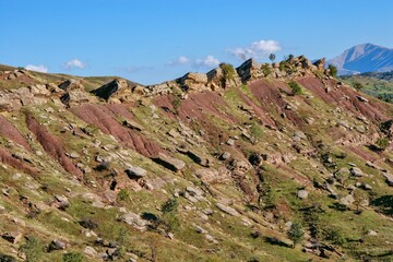 Layered rock formations of the Zagros Mountains, featuring distinctive red and green sedimentary strata under a clear sky in Kurdistan