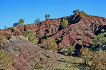 Layered rock formations of the Zagros Mountains, featuring distinctive red and green sedimentary strata under a clear sky in Kurdistan