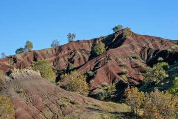 Layered rock formations of the Zagros Mountains, featuring distinctive red and green sedimentary strata under a clear sky in Kurdistan