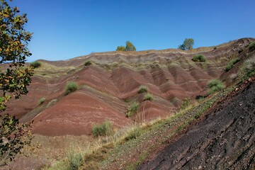 Layered rock formations of the Zagros Mountains, featuring distinctive red and green sedimentary strata under a clear sky in Kurdistan