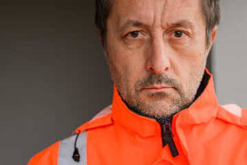 Serious civil engineer at construction site wearing orange safety jacket, focused professional portrait symbolizing responsibility and precision.