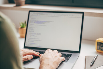 Close-up of male hands typing code on laptop computer at home office, concept of programming, software development, and remote digital work.
