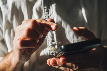 Closeup of male hands typing text message on smartphone, businessman in white shirt using mobile phone for communication in office, strong shadow and light contrast