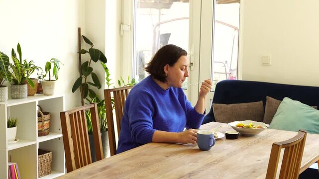Woman is eating launch at the table at the kitchen