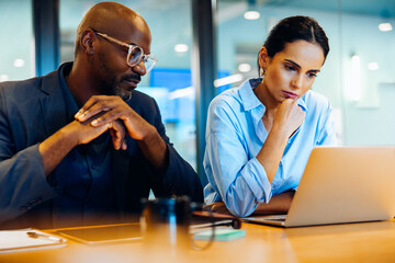 Two colleagues focused on a laptop during a thoughtful discussion
