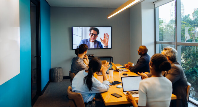 Colleagues in an office participate in a virtual meeting with a remote teammate