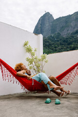 Fototapeta premium Couple relaxing in a hammock on a terrace with view of Corcovado mountain