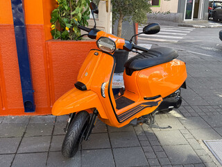 Bright orange scooter parked near colorful wall. Urban mobility, city lifestyle and cheerful street design.