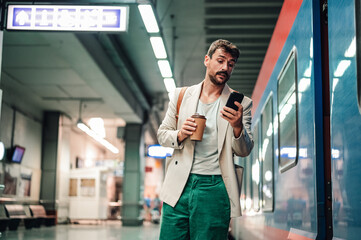 Man commuting to work checking phone while waiting for train