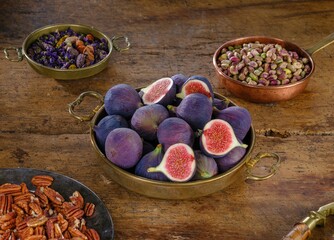 Figs fill a golden bowl, surrounded by pecans, pistachios, and dried flowers. The scene is set on a rustic wooden table, evoking a feeling of autumn and harvest time