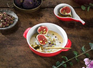 Halved figs are topped with pistachios and honey, nestled in vibrant red and white ceramic bowls. A small bowl of pistachios and figs rests nearby, on a dark wooden surface