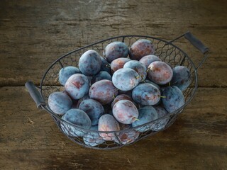 Basket overflows with ripe plums, their dusty bloom a soft contrast to the weathered wood beneath....