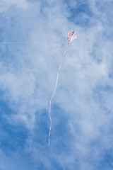 Kite flying high up in blue sky with long white streamer trailling from it