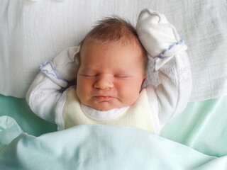 Newborn baby sleeping peacefully with arms raised with white mittens. Infant care and development, healthy baby sleep. Topics of childbirth, neonatology. Hypoallergenic, eco-friendly baby products.