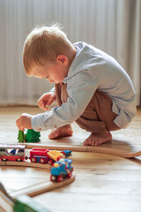 Boy crouching carefully places toy trees along wooden railway track. Concentration, creativity, focus and resilience through independent play with natural materials and simple sustainable design