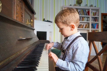 Young boy concentrating playing vintage piano at home in cozy living room with bookshelves. World Music Day. Day of Education. Early childhood development and homeschooling. Talent and Discipline