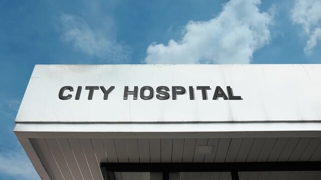 City Hospital word sign prominently displayed on the large, institutional facade of a major medical center beneath a clear blue sky, signifying a primary healthcare facility serving the city
