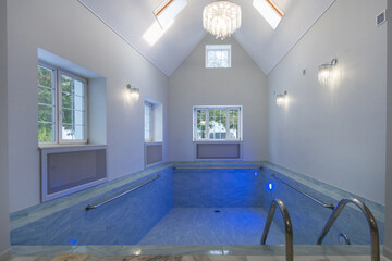 An elegant indoor swimming pool with bright lighting, large windows and a luxurious chandelier. A space for relaxation and enjoyment at any time of the day.