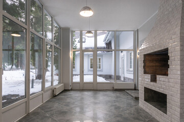 A spacious room with a white brick fireplace and large windows offering a beautiful view of the winter landscape.