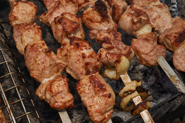 Large pieces of pork being grilled on skewers over hot charcoal. Delicious barbecue with a golden crust cooking outdoors during a picnic or countryside gathering.