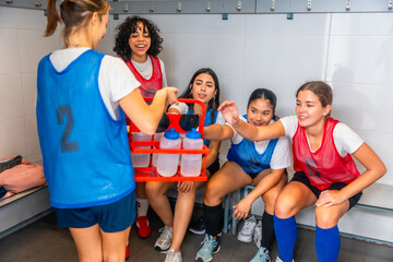 Diverse girls soccer team sharing water in locker room