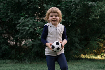 Cute smiling girl playing football with soft children's ball in the park, selective focus, real photo.