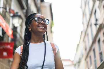 Smiling Latina woman with braided hair using an analog camera on the street