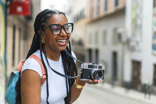 Smiling Latina woman with braided hair using an analog camera on the street