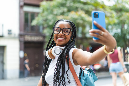 Smiling Latina woman with braided hair on the street using her smartphone