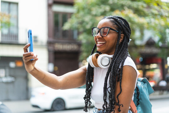 Smiling Latina woman with braided hair standing on the street using her smartphone