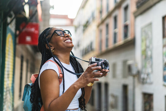 Smiling Latina woman with braided hair using an analog camera on the street