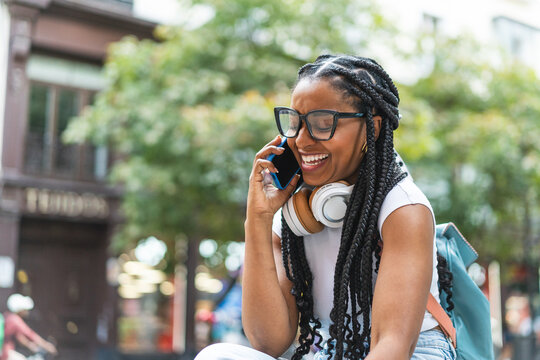 Smiling Latina woman with braided hair standing on the street using her smartphone