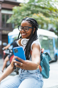 Smiling Latina woman with braided hair standing on the street using her smartphone